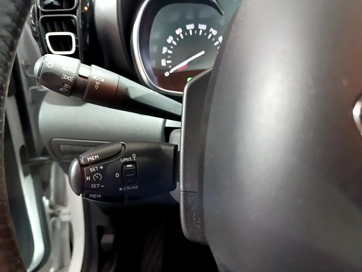 Gros plan sur la commande de régulateur de vitesse à gauche du volant dans l’habitacle d’un Citroën C3 Aircross blanc 2019.