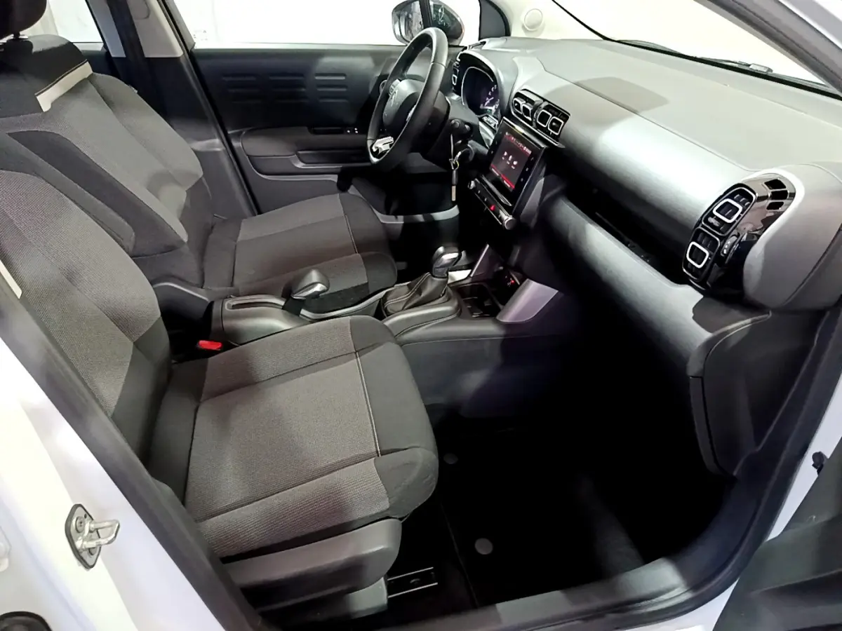 Vue intérieure côté conducteur de la Citroën C3 Aircross blanche, montrant sièges tissu gris et tableau de bord avec écran tactile.