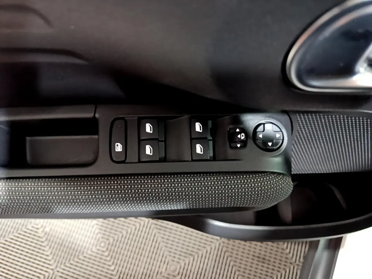 Gros plan sur la commande des vitres et rétroviseurs côté gauche intérieur d'une Citroën C3 Aircross blanche.