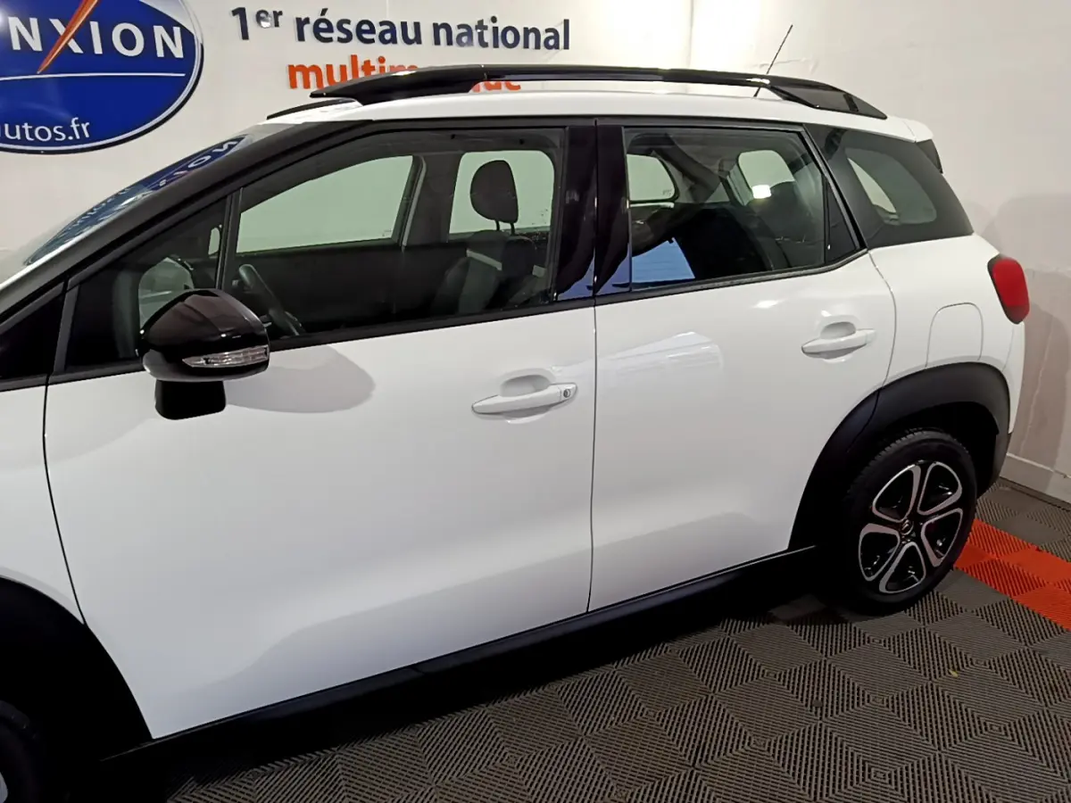 Vue latérale droite d'un Citroën C3 Aircross blanc avec rétroviseurs noirs et barres de toit noires.