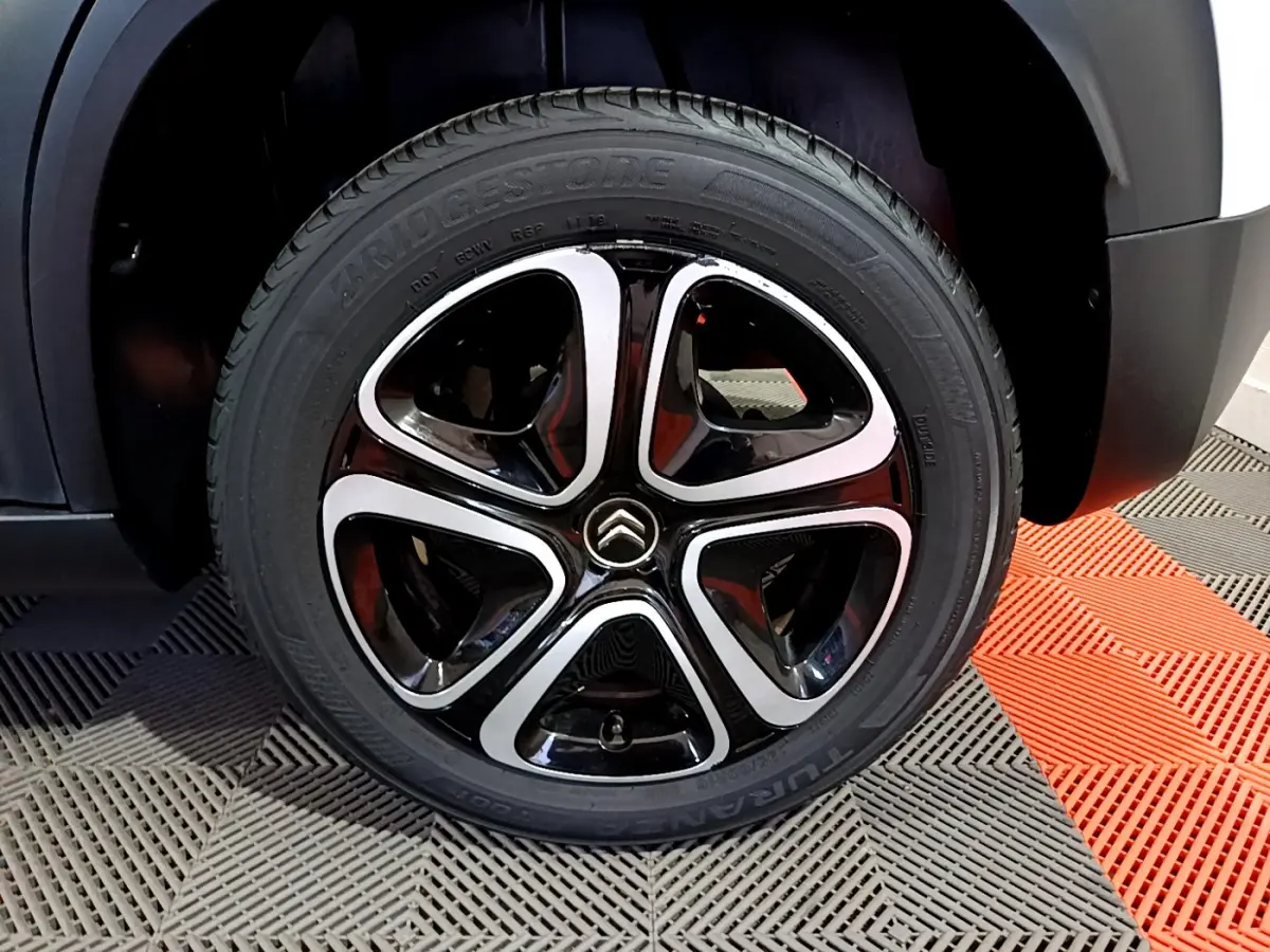Gros plan sur la roue avant droite du Citroën C3 Aircross blanc, jante alliage noire et argentée au design moderne.