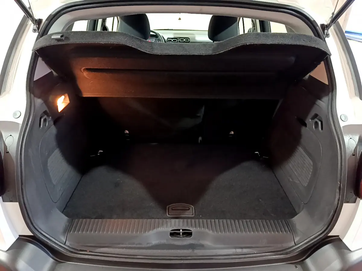 Coffre ouvert vu de l'arrière d'une Citroën C3 Aircross blanche, espace de chargement noir avec tablette relevée.