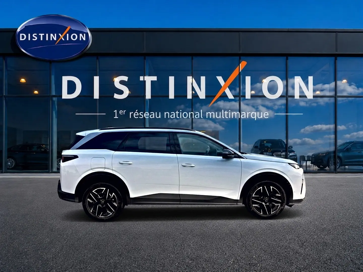 Vue de profil côté gauche d’un Peugeot 5008 blanc avec jantes alliage noires devant une vitrine Distinxion.