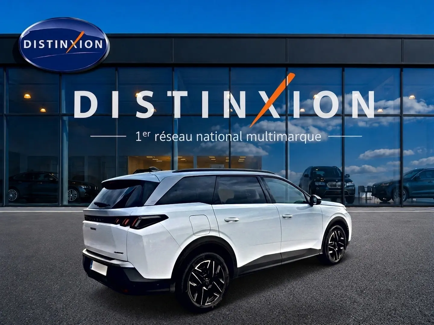 Peugeot 5008 Hybrid blanc en 3/4 arrière droit, avec jantes noires et toit noir, devant un bâtiment vitré Distinxion.