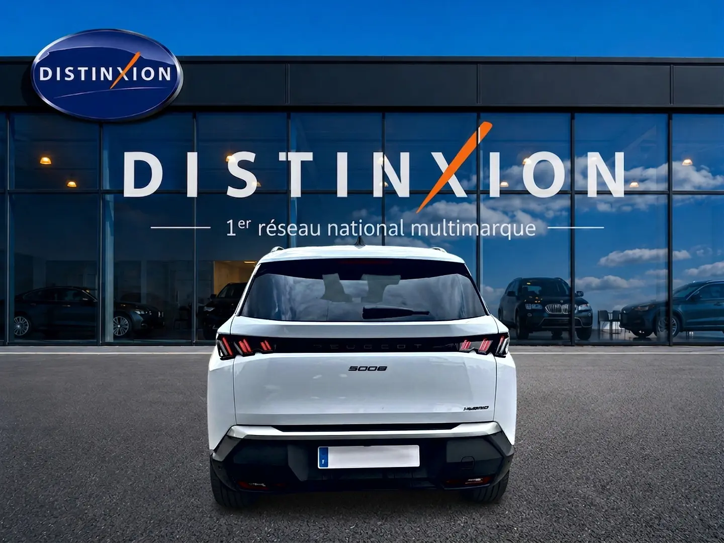 Vue arrière d'un Peugeot 5008 blanc hybride 2025 avec feux LED distinctifs, stationné devant une vitrine Distinxion.