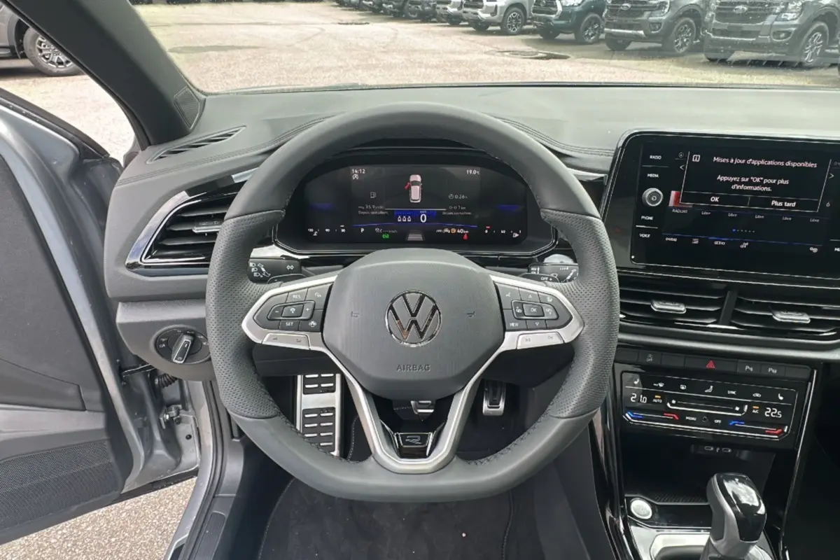 Vue intérieure centrée sur le volant du Volkswagen T-Roc gris pyrite 2025, avec tableau de bord numérique et écran tactile.