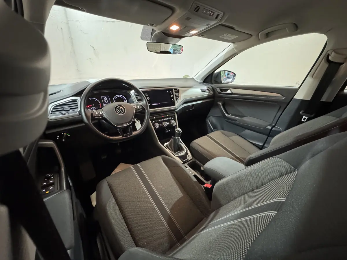 Intérieur de Volkswagen T-Roc 1.6 TDI 2021 vu côté conducteur, tableau de bord moderne et sièges tissu gris foncé.