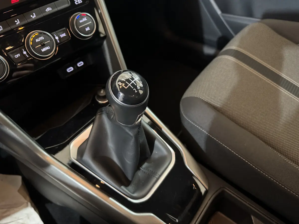 Gros plan sur la commande de boîte manuelle noire et la partie avant du siège tissu gris dans l’habitacle du Volkswagen T-Roc.