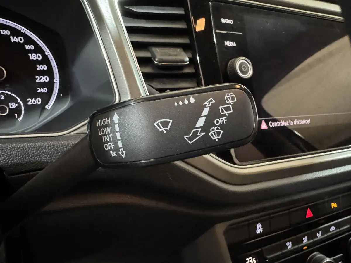Gros plan sur la commande des essuie-glaces dans l’habitacle du Volkswagen T-Roc gris foncé, tableau de bord et écran tactile visibles.