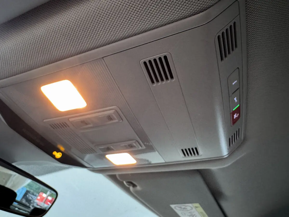 Plafonnier intérieur allumé vu de dessous dans un Volkswagen T-Roc gris foncé, avec commandes et aérations visibles.