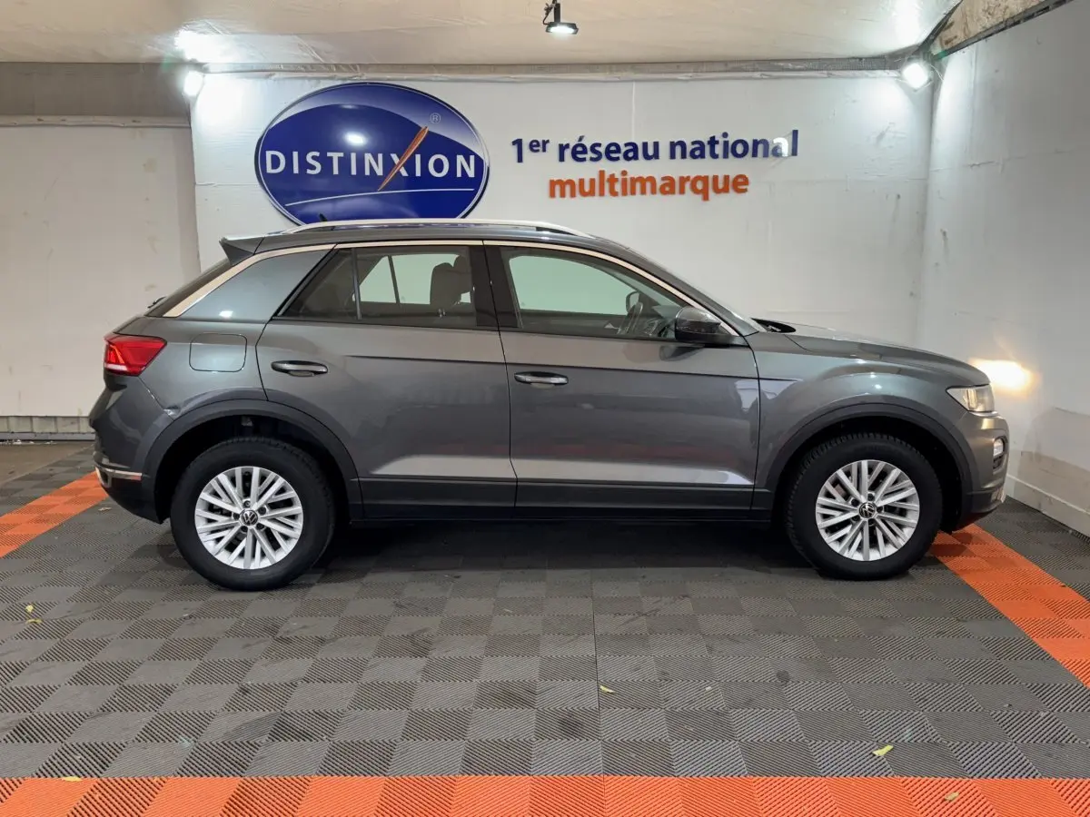 Profil droit d'un Volkswagen T-Roc gris foncé 2021 garé en intérieur avec jantes alliage et rails de toit noirs.