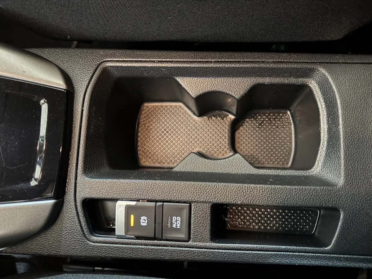 Gros plan sur la console centrale noire du Volkswagen T-Roc 1.6 TDI, avec porte-gobelets et frein à main électrique activé.