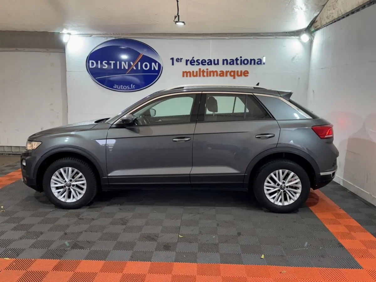 Profil côté gauche d'un Volkswagen T-Roc gris foncé 2021 stationné en intérieur avec jantes alliage visibles.