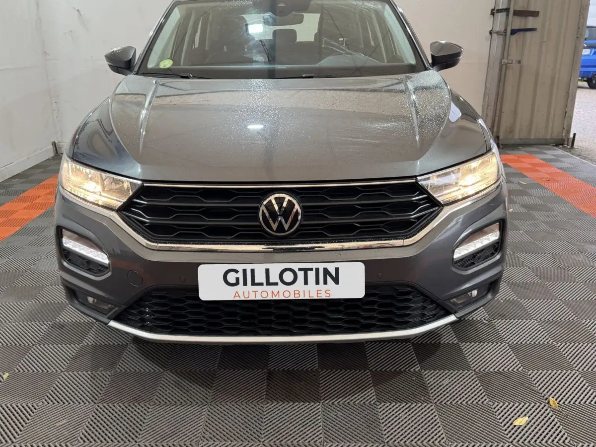 Vue avant rapprochée du Volkswagen T-Roc gris foncé 2021 avec calandre noire et phares allumés.