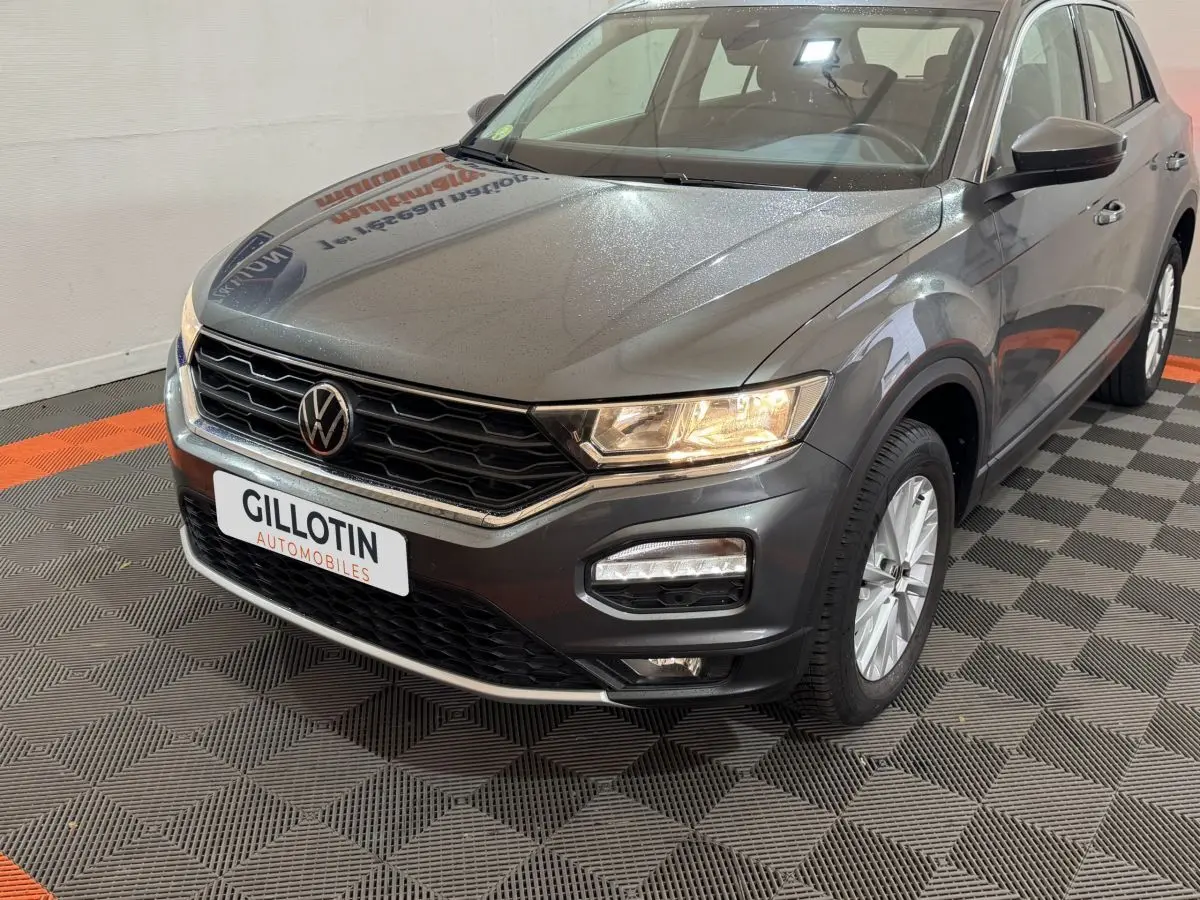Vue 3/4 avant droit d’un Volkswagen T-Roc gris foncé avec phares allumés et calandre noire distinctive.
