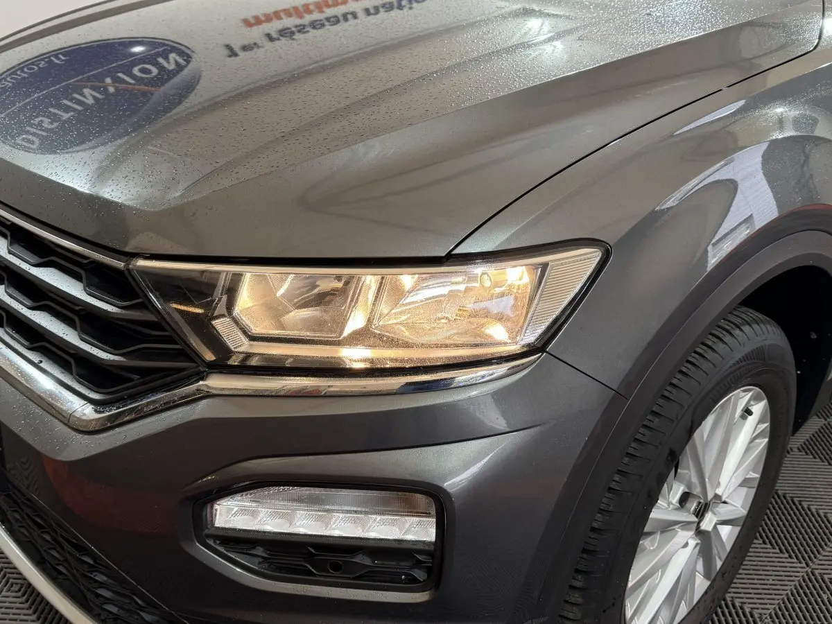 Gros plan sur l'avant droit gris foncé du Volkswagen T-Roc 1.6 TDI 115, mettant en valeur le phare allumé et la roue.