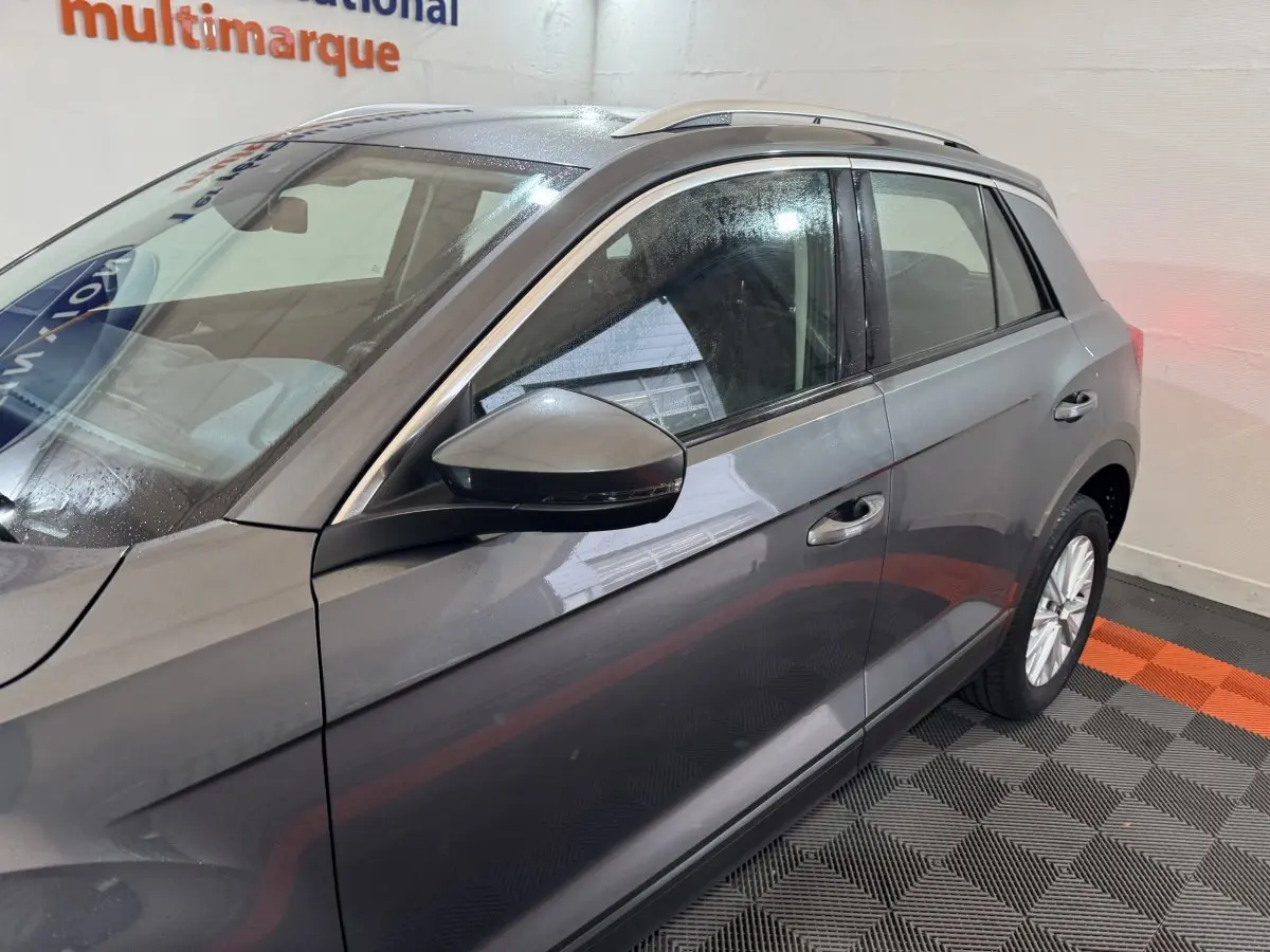 Vue côté gauche du Volkswagen T-Roc gris foncé, mettant en valeur la porte avant et le rétroviseur avec clignotant intégré.