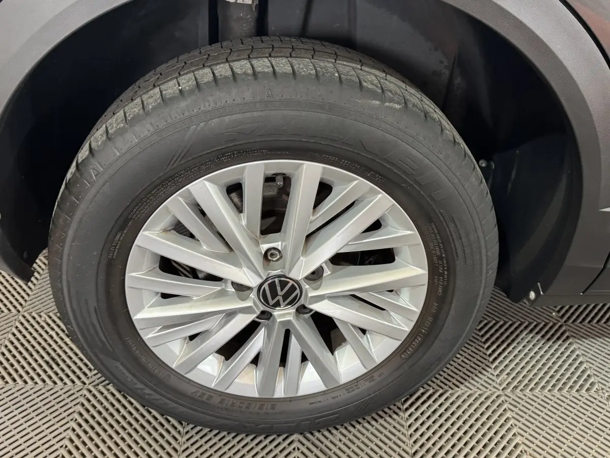 Gros plan sur la roue avant droite d’un Volkswagen T-Roc gris foncé, mettant en valeur la jante alliage et le logo VW.