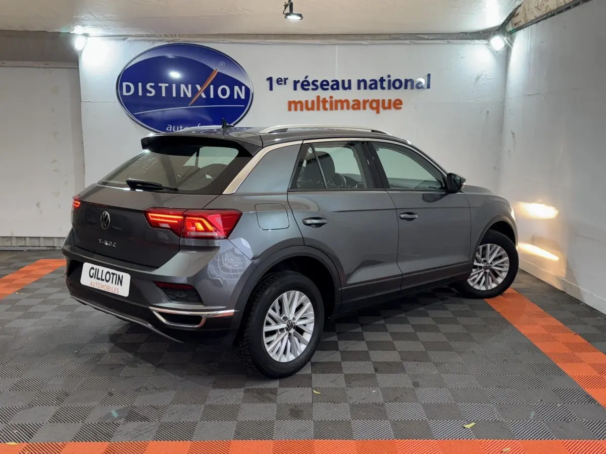 Volkswagen T-Roc gris foncé vue 3/4 arrière droit en intérieur avec feux arrière allumés.