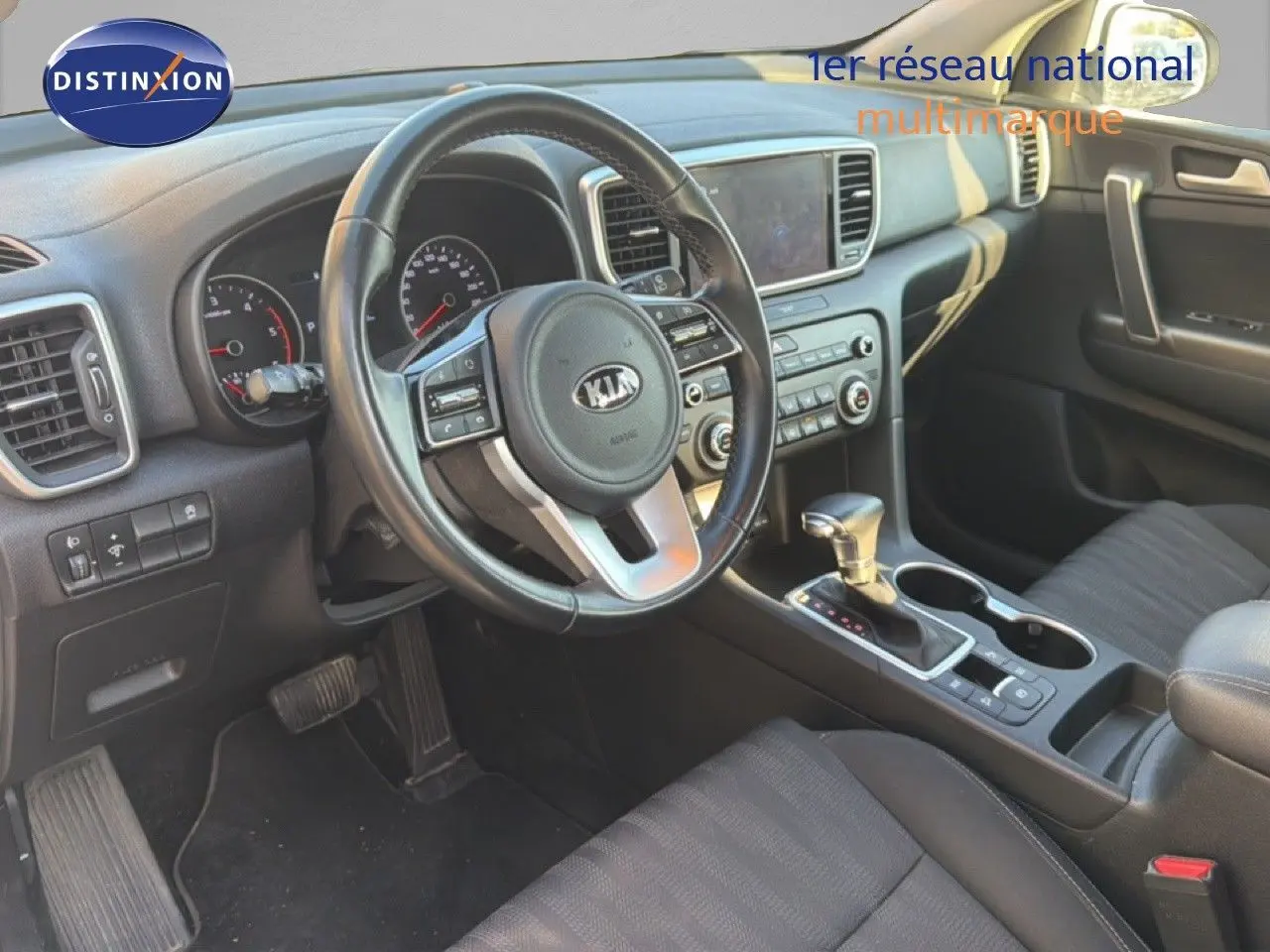 Vue intérieure côté conducteur du Kia Sportage 2021, tableau de bord noir avec volant multifonction et console centrale.