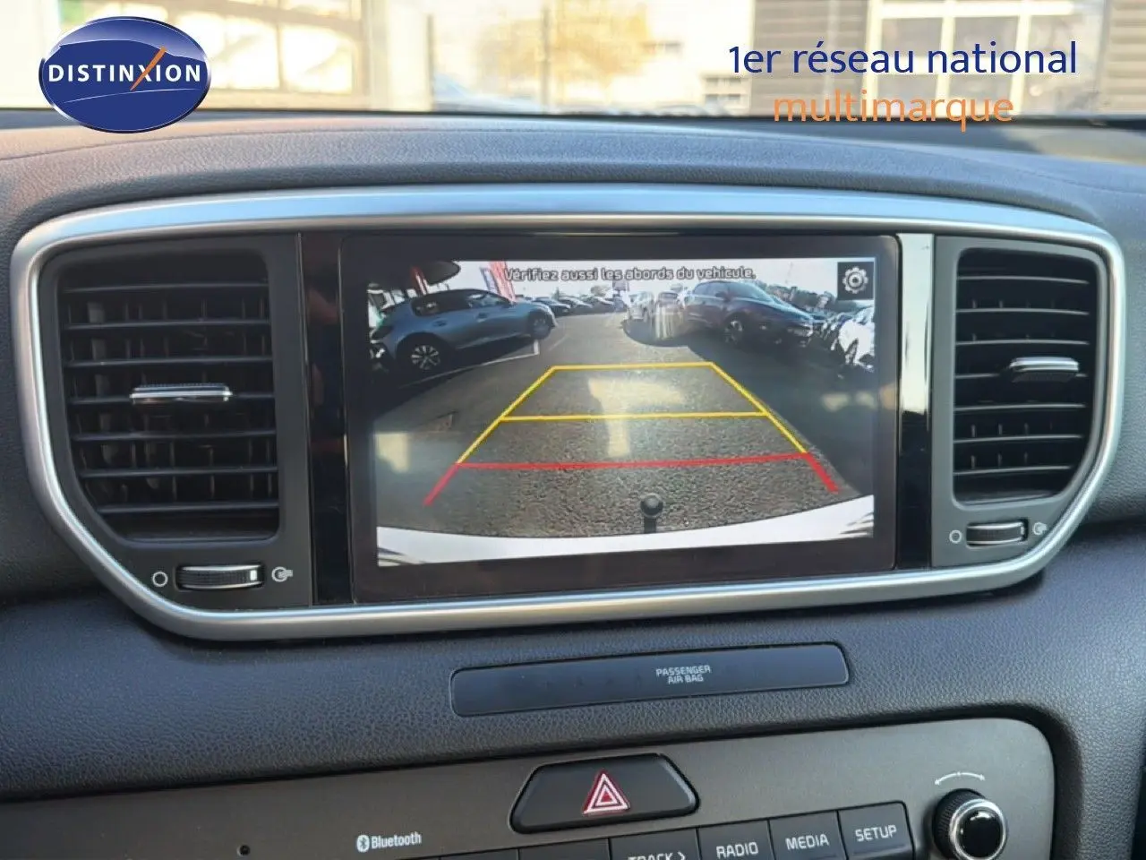 Vue intérieure du tableau de bord du Kia Sportage blanc nacré, affichant la caméra de recul sur l'écran central.