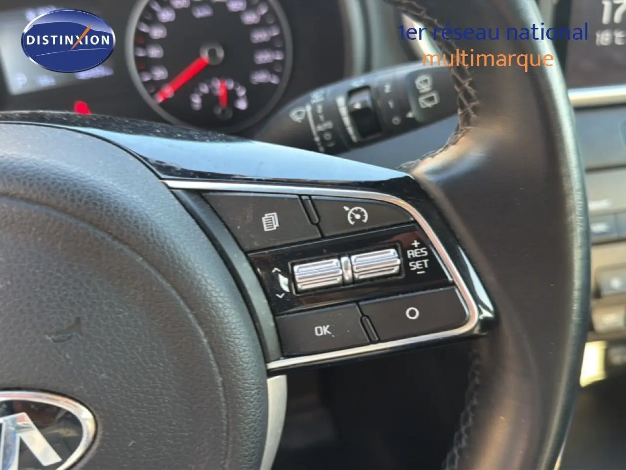 Gros plan sur les commandes au volant en cuir noir du Kia Sportage blanc nacré, avec tableau de bord en arrière-plan flou.