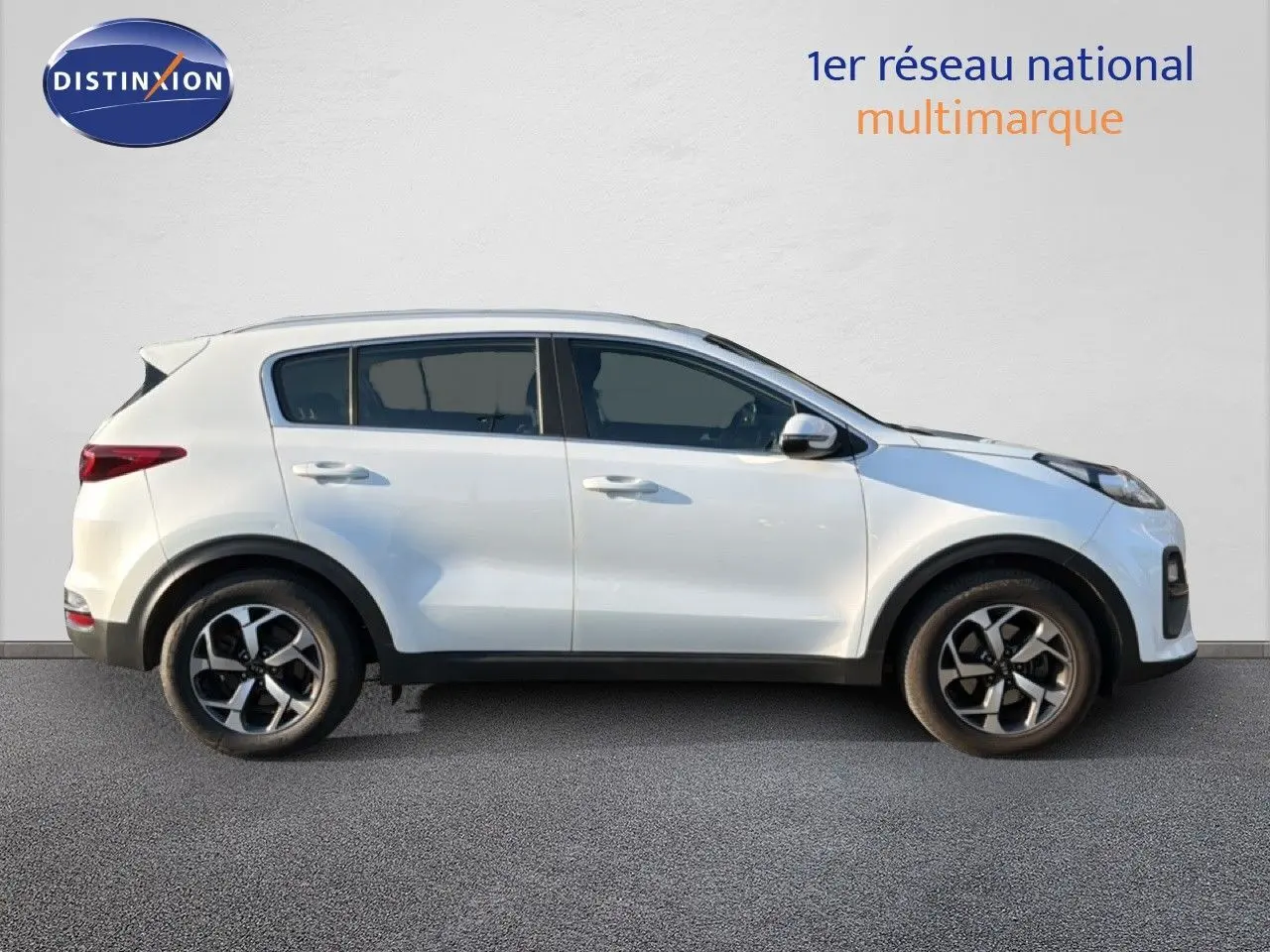 Vue de profil côté gauche d’un KIA Sportage blanc nacré 2021 avec jantes alliage bicolores et carrosserie compacte.