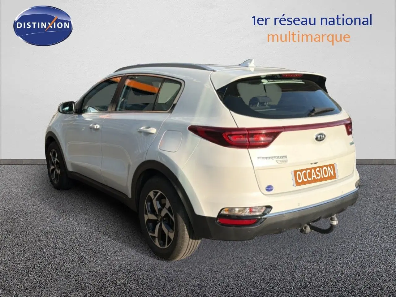 Vue 3/4 arrière droite d'un Kia Sportage blanc nacré avec attelage et jantes bi-ton.