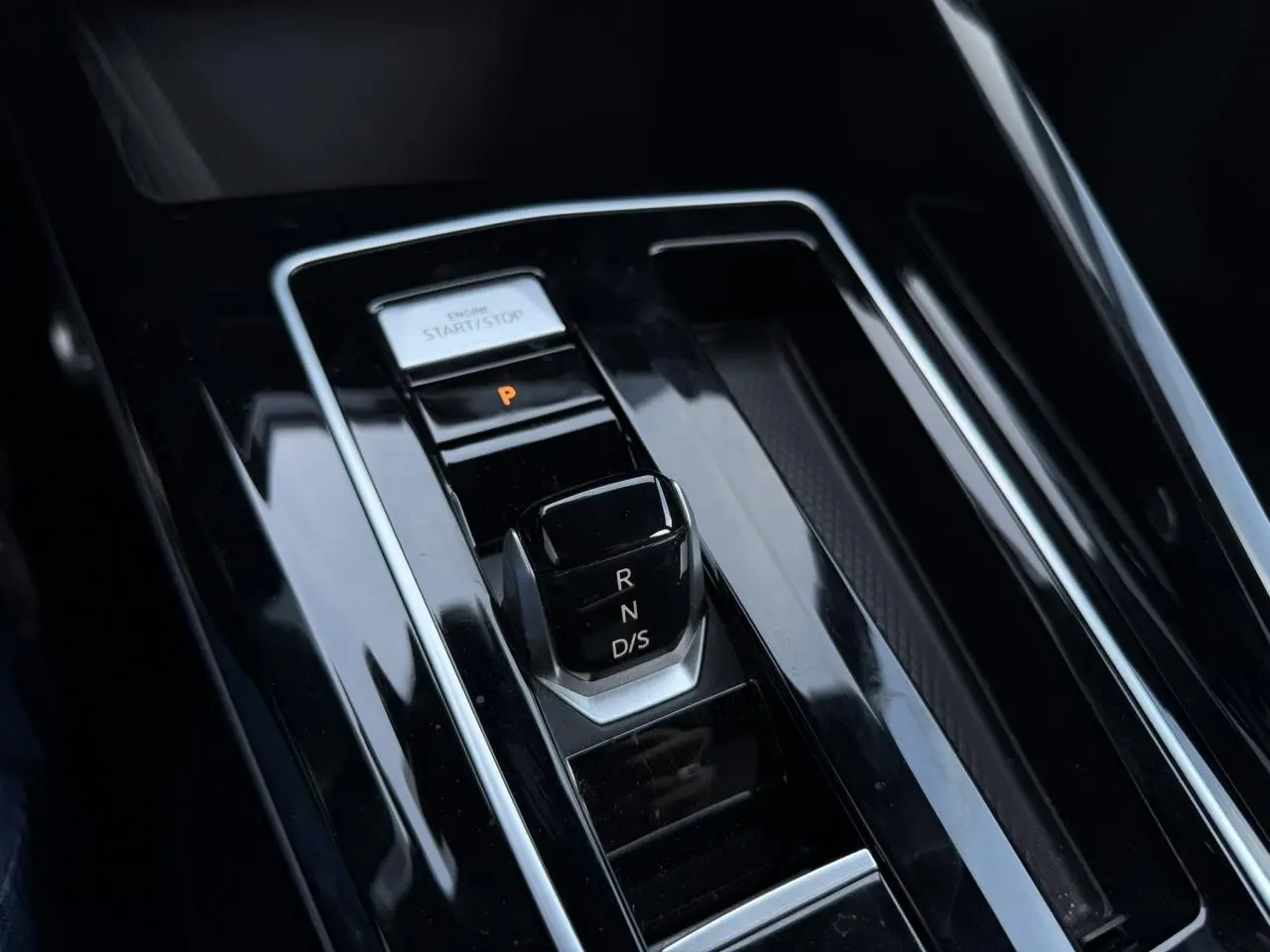 Gros plan sur la console centrale noire brillante avec sélecteur de boîte auto et bouton start/stop dans une Volkswagen Golf 8 R-Line.