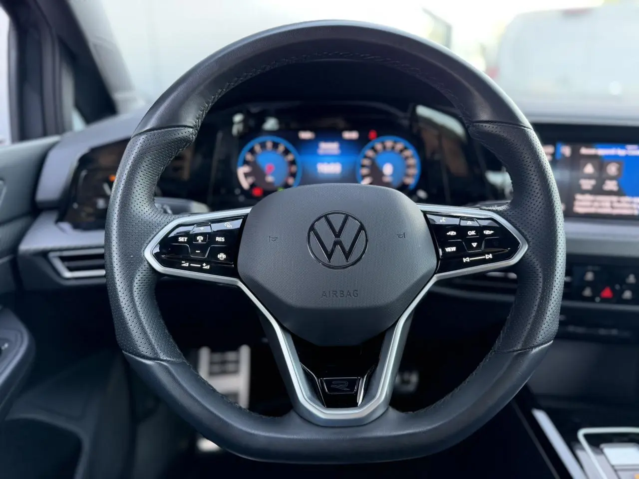 Vue rapprochée du volant cuir multifonction noir avec logo Volkswagen, tableau de bord numérique et écran tactile en arrière-plan.