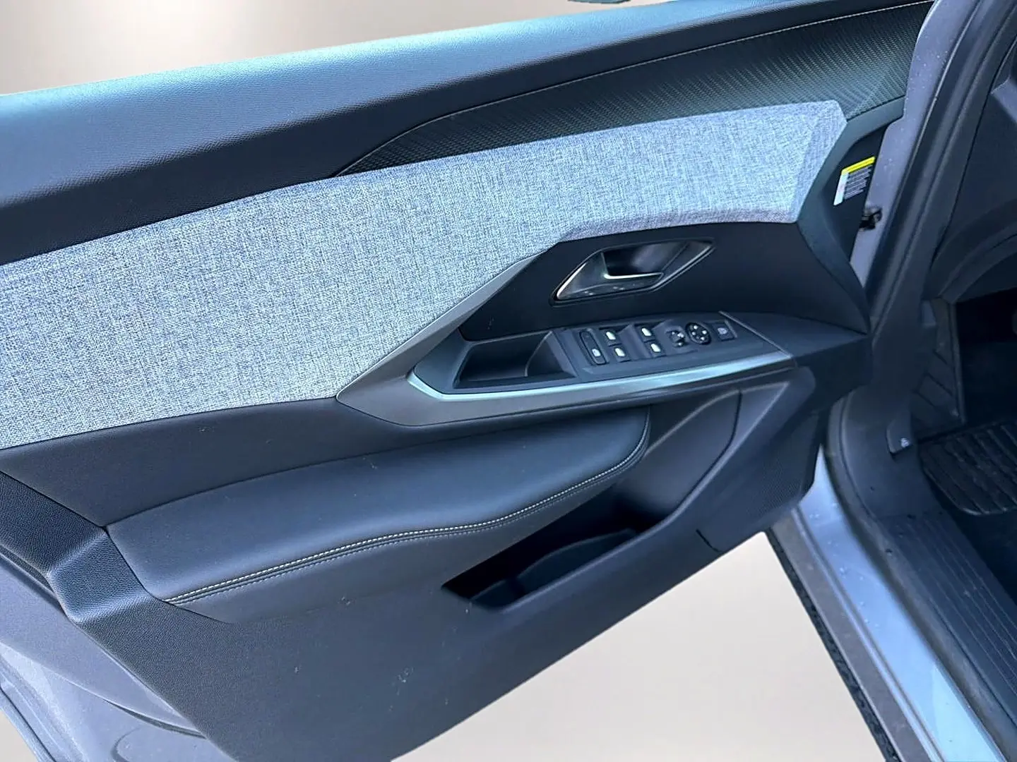 Vue rapprochée de la porte avant gauche du Peugeot 5008 gris artense, montrant les commandes des vitres et le revêtement tissu.