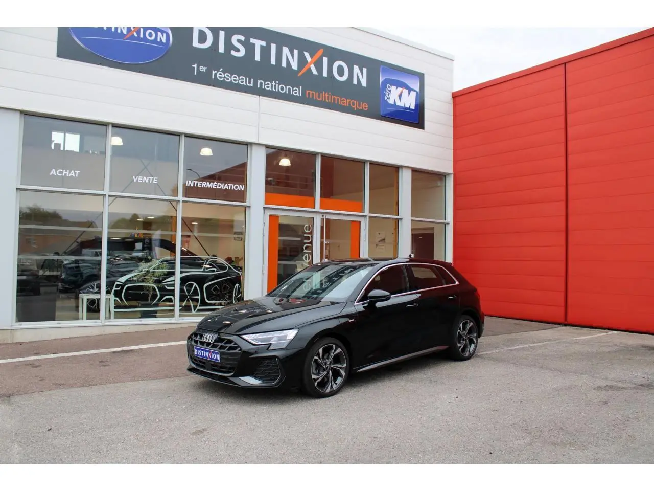 Audi A3 Sportback noir mito metal vue 3/4 avant avec jantes 5 branches et calandre S line devant un bâtiment rouge.