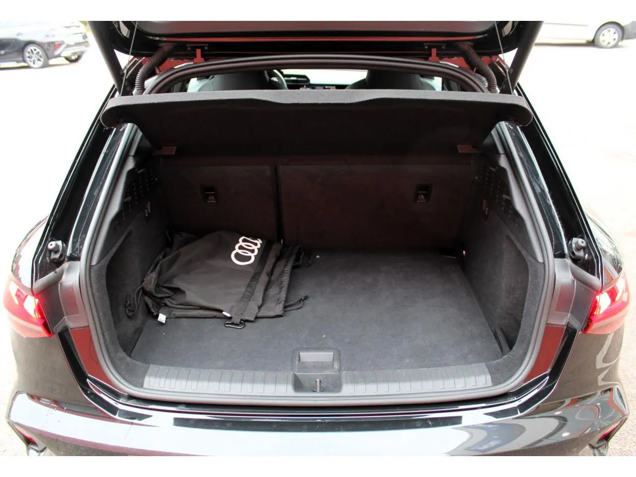 Coffre ouvert vu de l'arrière d'une Audi A3 Sportback noir Mito Metal avec sac Audi à l'intérieur.