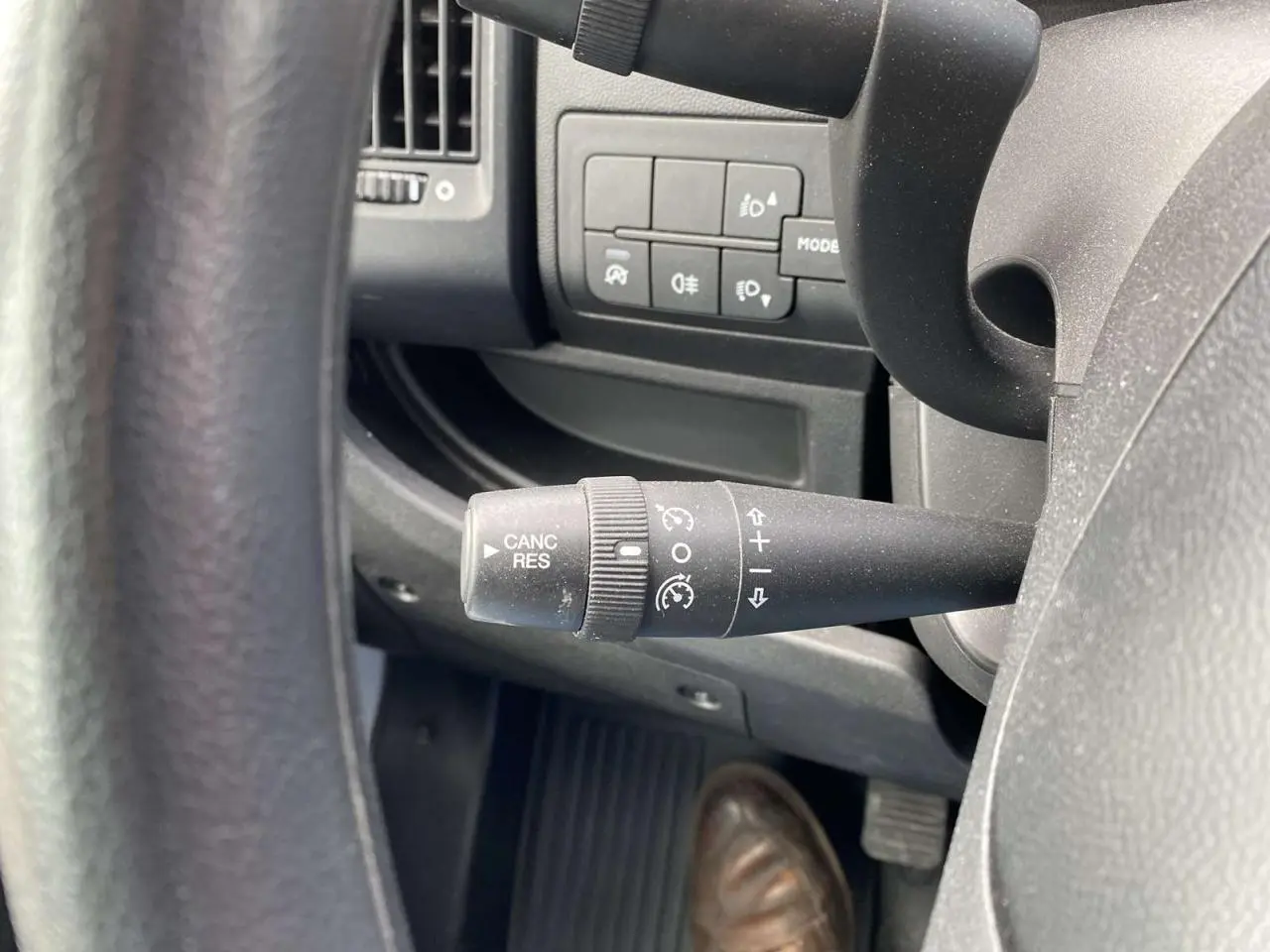 Gros plan sur la commande de régulateur de vitesse noire à gauche du volant dans l'habitacle d'un Opel Movano blanc.