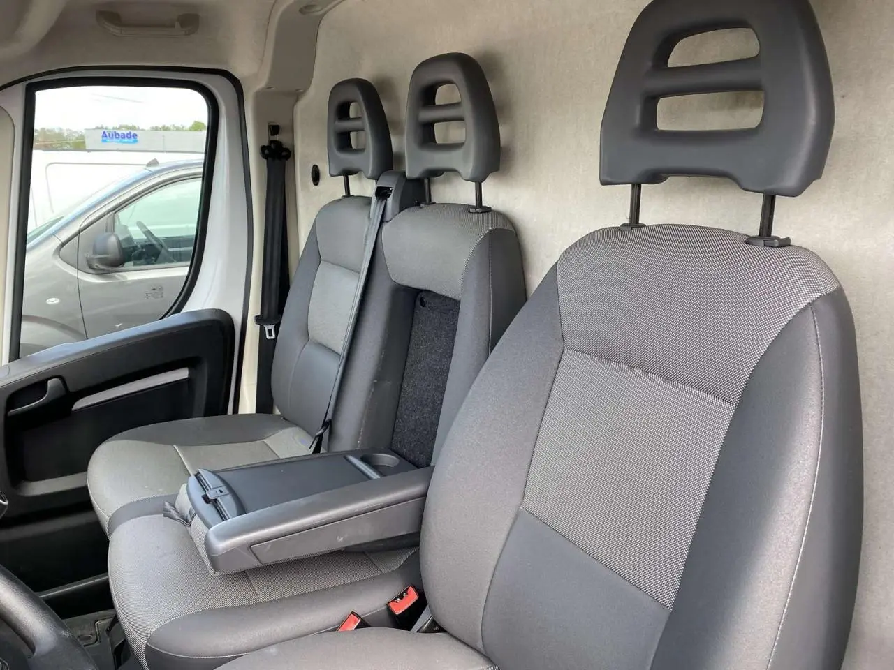 Intérieur du fourgon Opel Movano blanc 2022, vue côté gauche sur les sièges avant gris avec accoudoir conducteur.