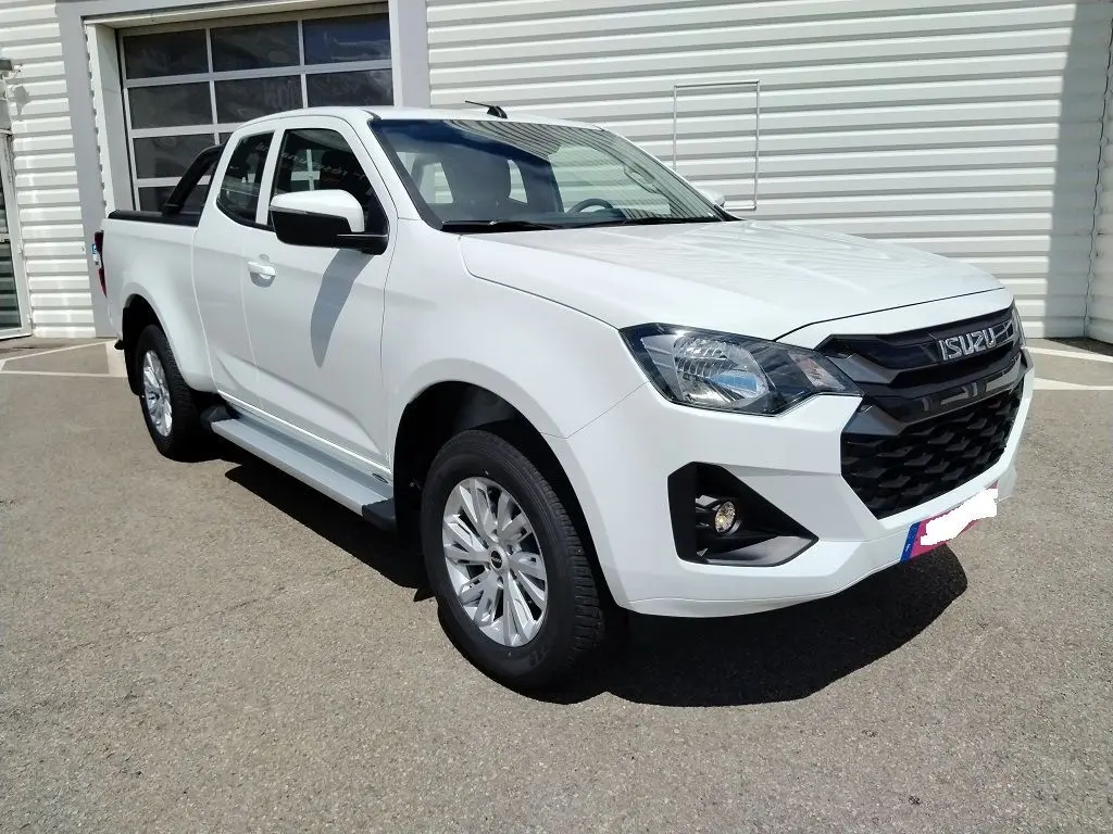 Vue 3/4 avant d'un Isuzu D-MAX blanc avec arceau et couvre benne roulant, stationné devant un bâtiment Distinxion.