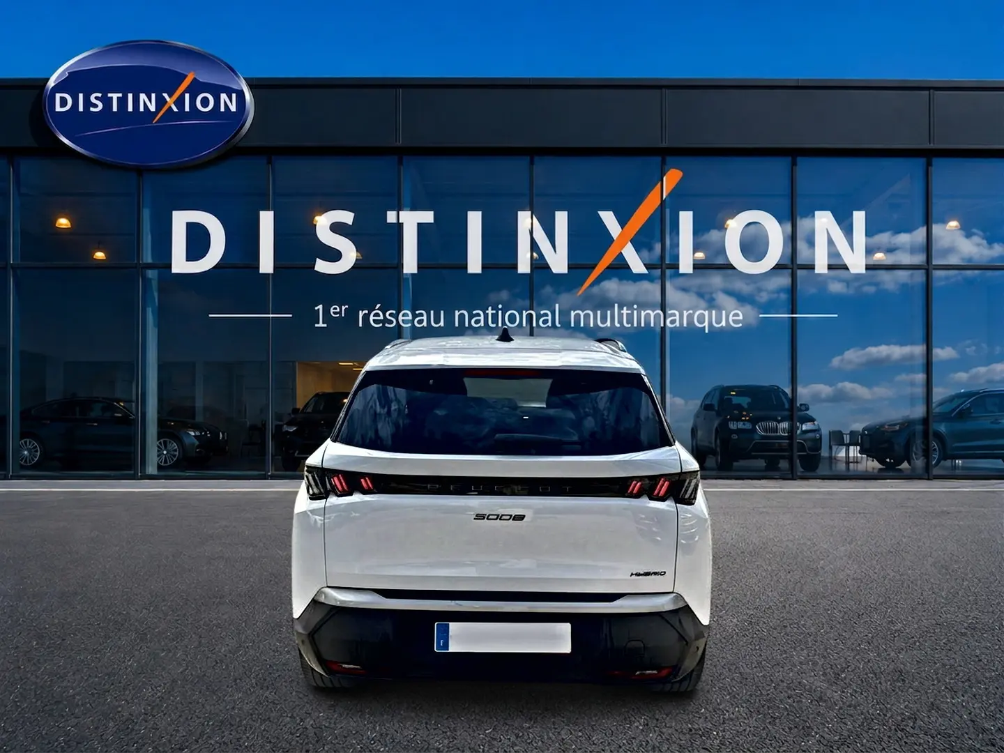 Vue arrière d’un Peugeot 5008 Hybrid blanc garé devant une vitrine avec logo Distinxion.