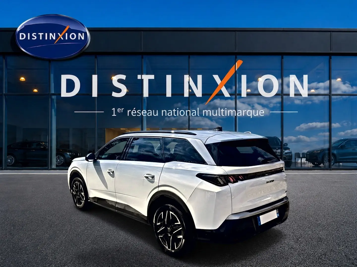 Peugeot 5008 blanc vue 3/4 arrière droit, jantes alu noires, vitres arrière surteintées, devant showroom Distinxion.