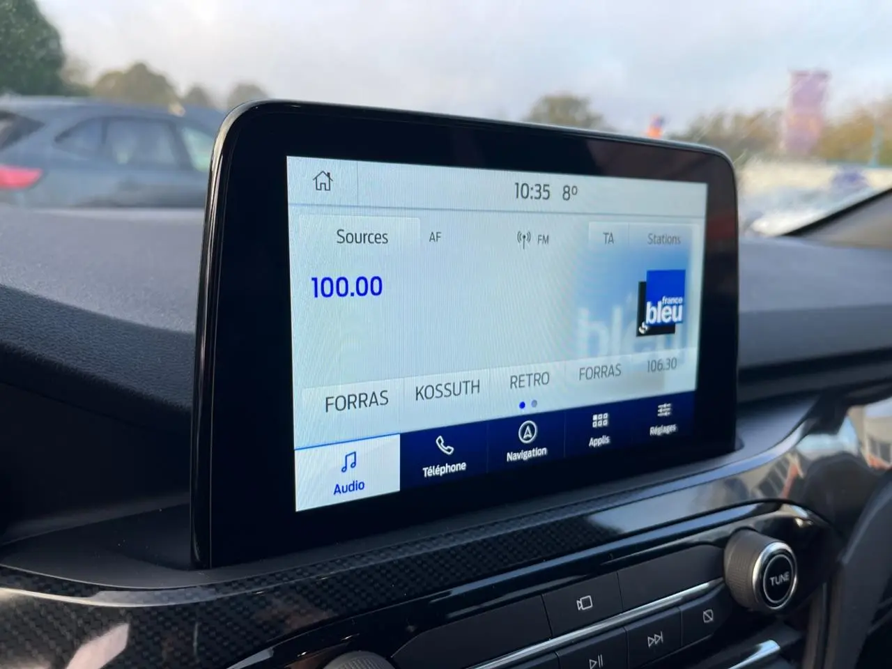 Écran tactile central du Ford Kuga 2022 affichant la radio, avec tableau de bord noir et finition carbone.