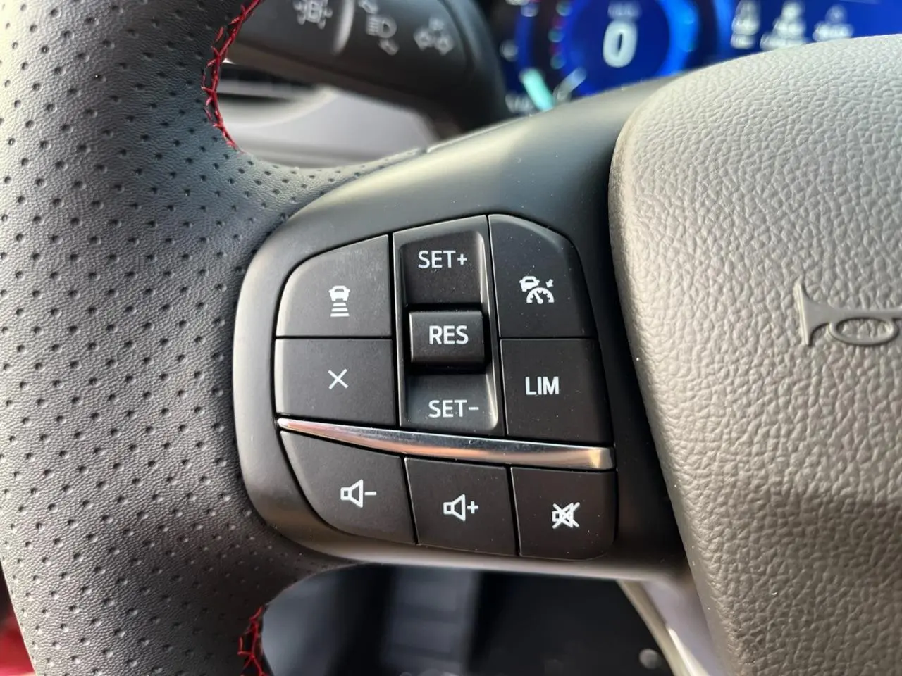 Gros plan sur les commandes de régulateur de vitesse et volume au volant perforé du Ford Kuga 1.5 EcoBoost rouge Lucifer.