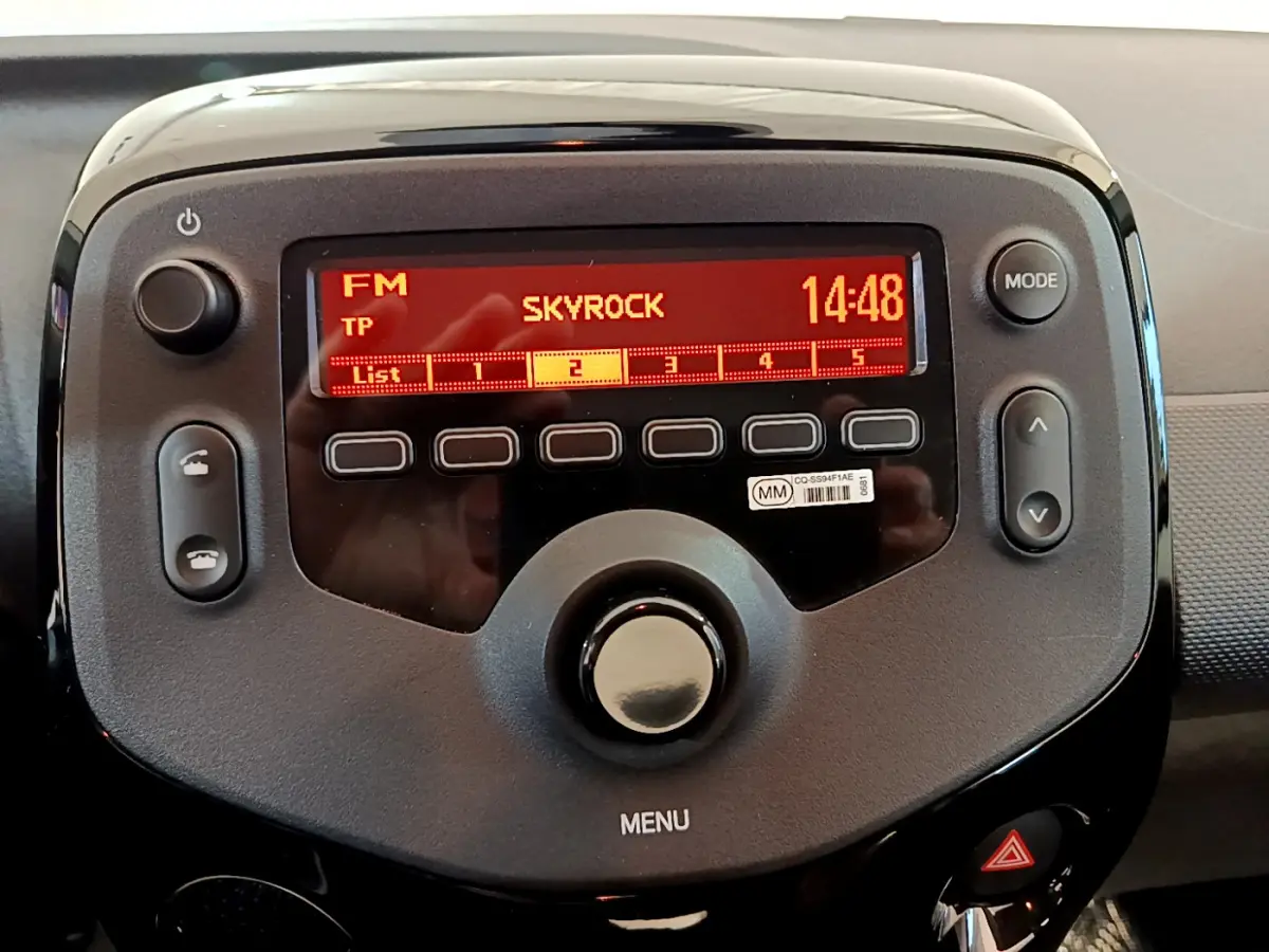 Vue rapprochée de la radio digitale rouge allumée dans le tableau de bord noir de la Citroën C1 blanche de 2020.