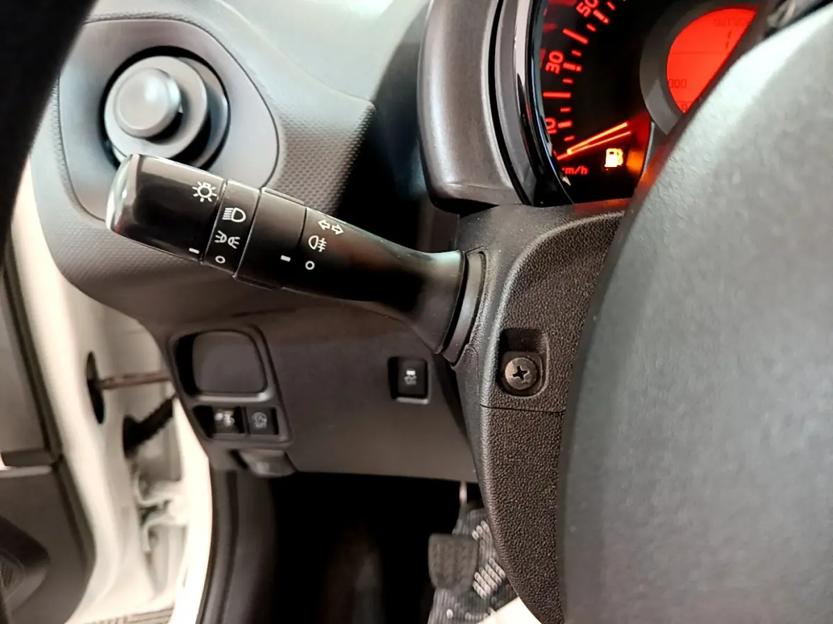 Vue rapprochée du commodo d'éclairage à gauche du volant d'une Citroën C1 blanche, tableau de bord rouge en arrière-plan.