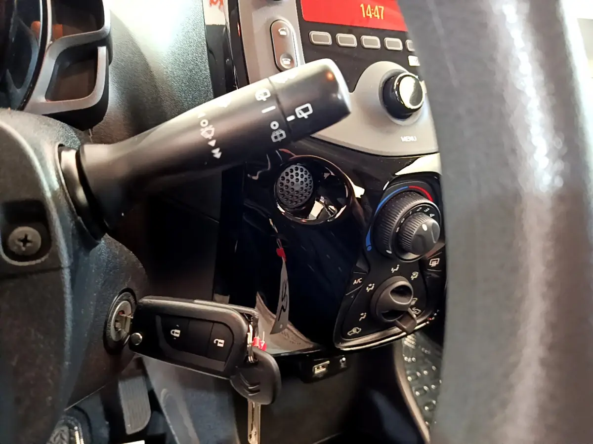 Gros plan sur le tableau de bord noir et la commande de climatisation de la Citroën C1 blanche, avec clé insérée.