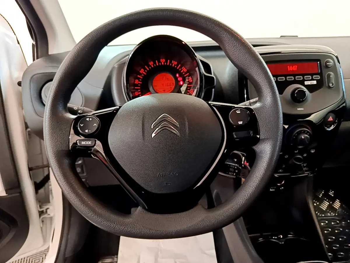 Vue intérieure centrée sur le volant noir de la Citroën C1 blanche, avec tableau de bord et commandes visibles.