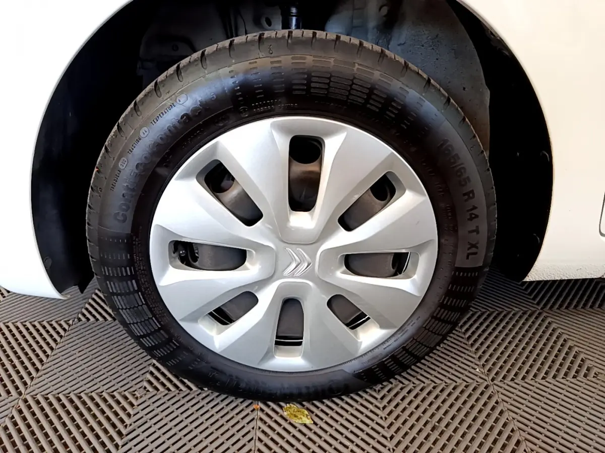 Gros plan sur la roue avant droite d'une Citroën C1 blanche avec enjoliveur argenté et logo Citroën central.