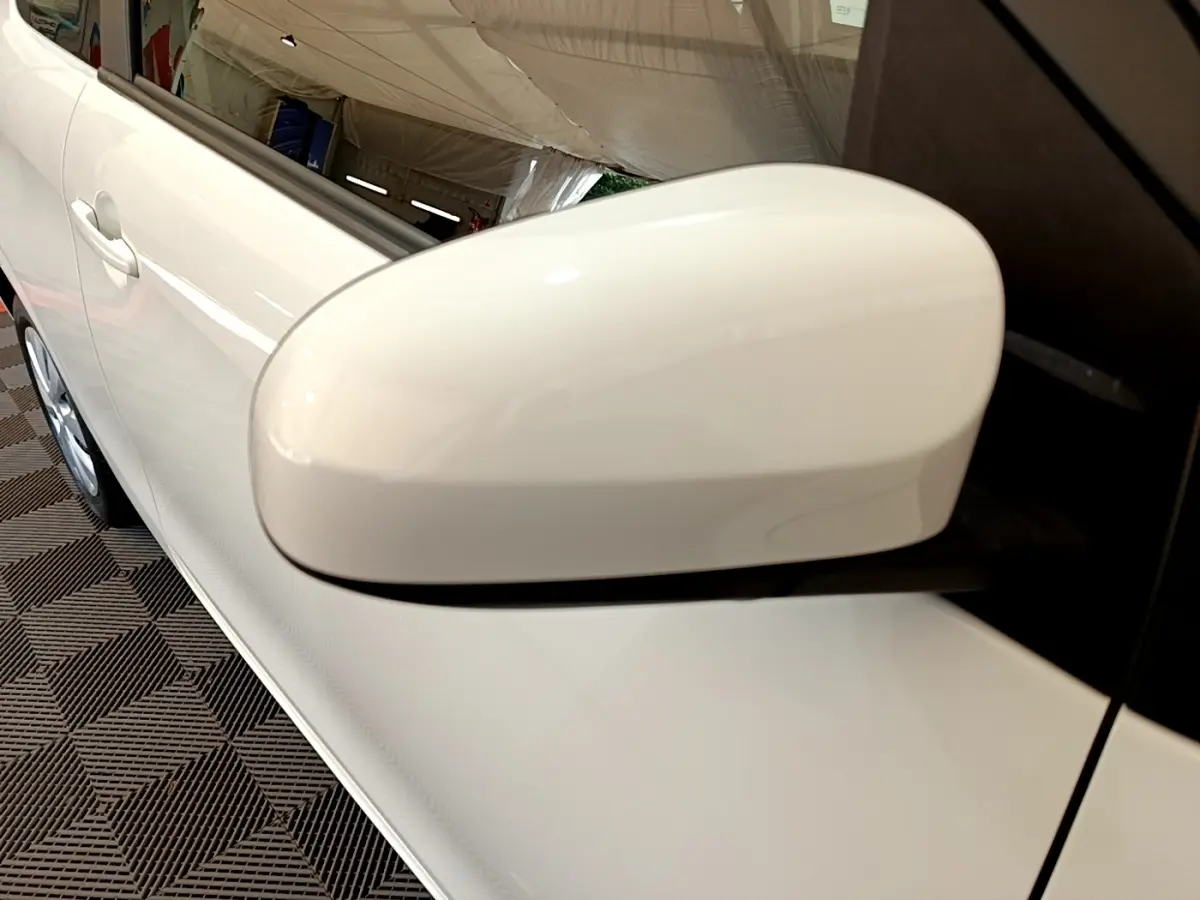 Gros plan sur le rétroviseur côté droit blanc d'une Citroën C1 blanche, avec une partie de la porte visible.