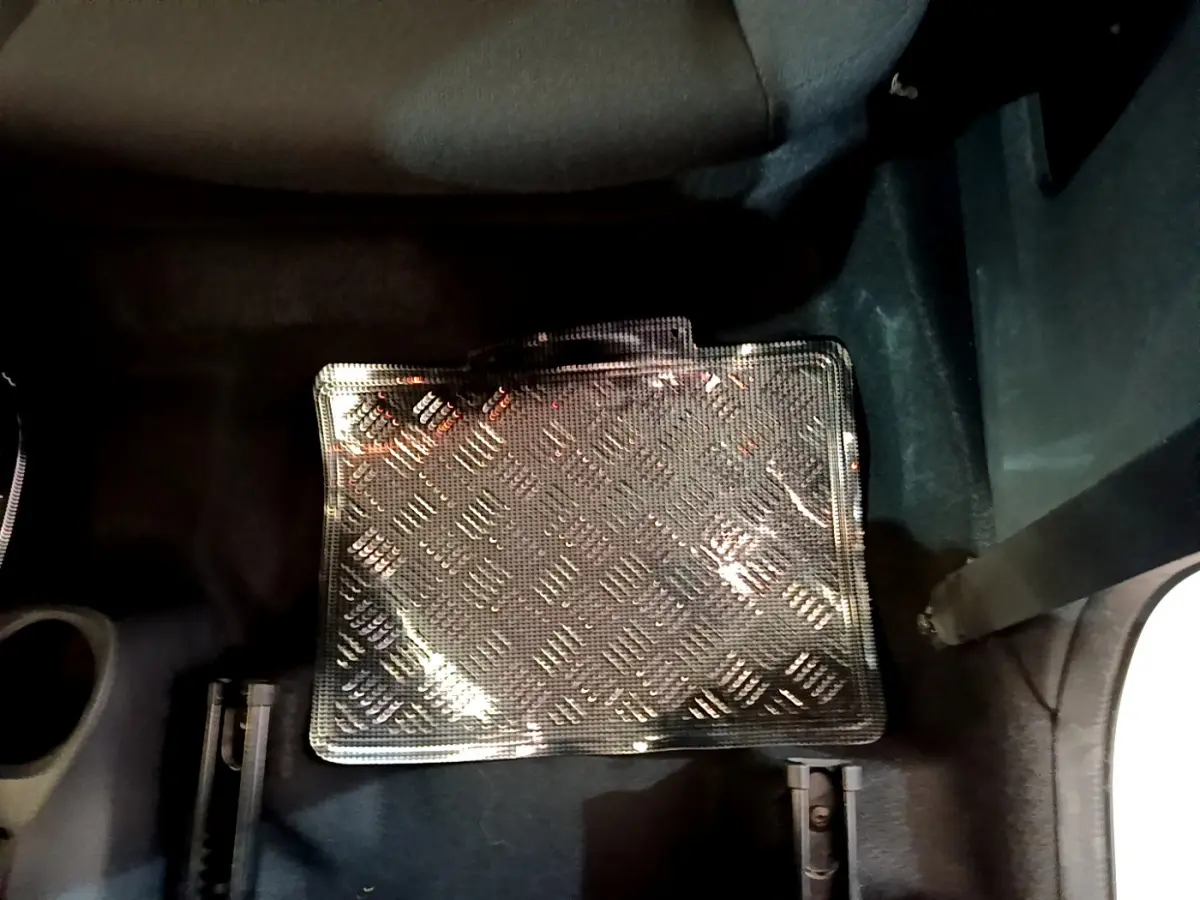 Gros plan sur le tapis de sol noir à motif damier dans l'habitacle d'une Citroën C1 blanche, côté passager arrière.