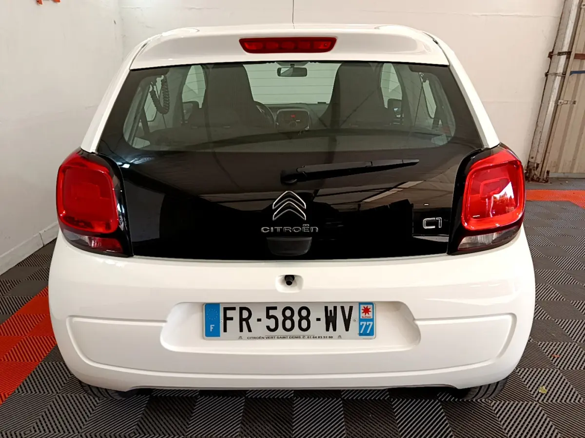 Vue arrière d'une Citroën C1 blanche avec hayon noir et feux arrière rouges dans un garage.