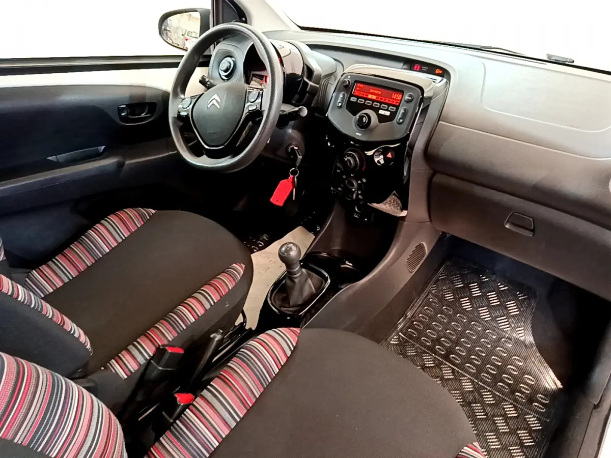 Vue intérieure avant droite du Citroën C1 2020, volant noir, sièges tissu rayé rouge et noir, console centrale avec radio.