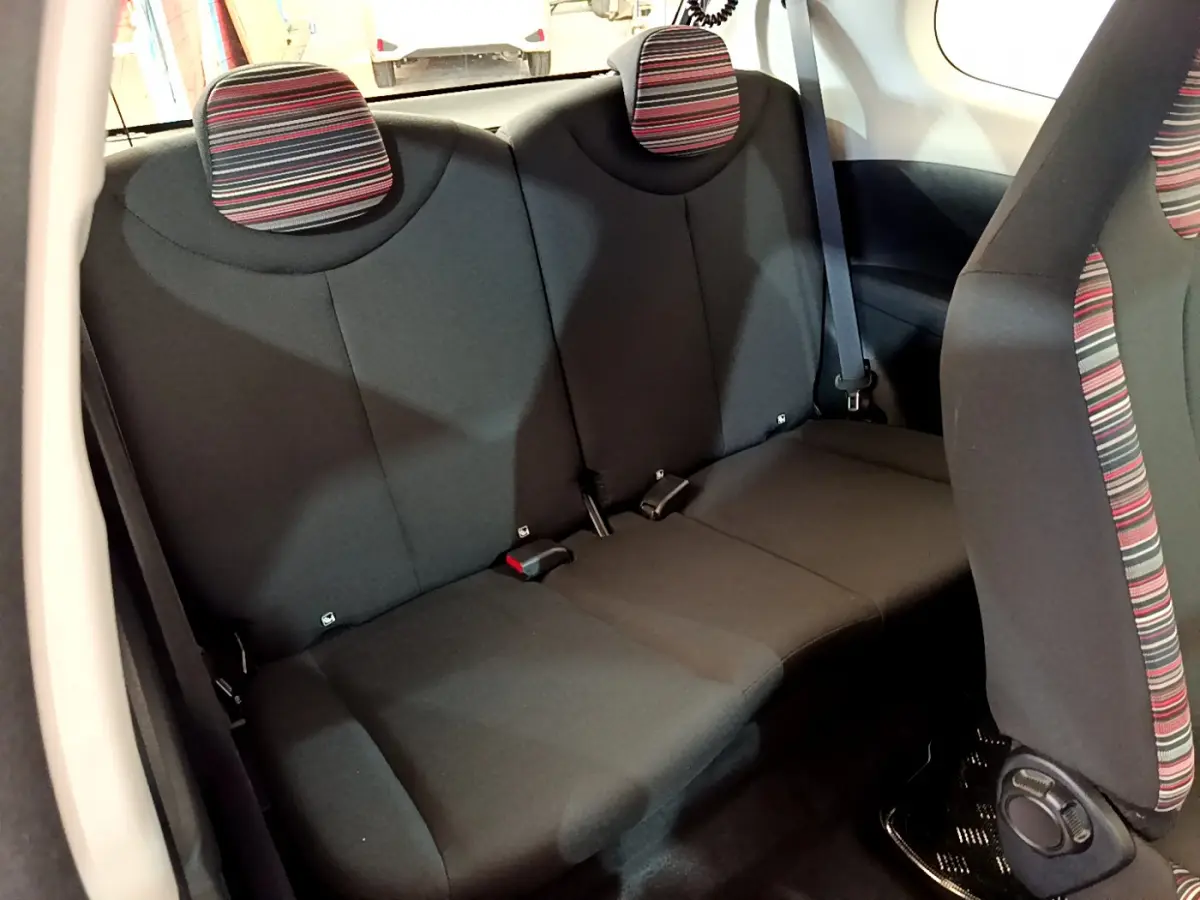 Vue intérieure arrière de la banquette noire avec appuie-têtes rayés rouge et gris de la Citroën C1 blanche.